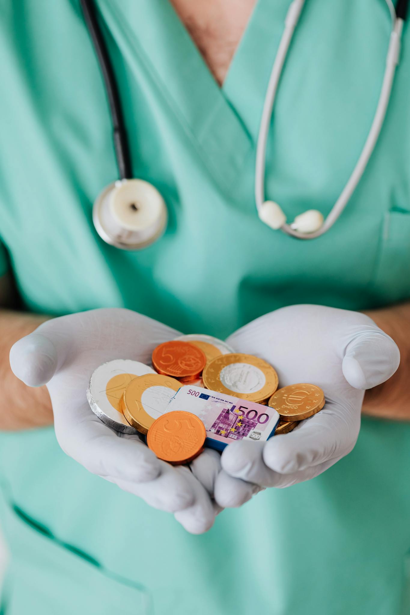 From above crop faceless doctor with stethoscope on shoulders holding in hands chocolate coins